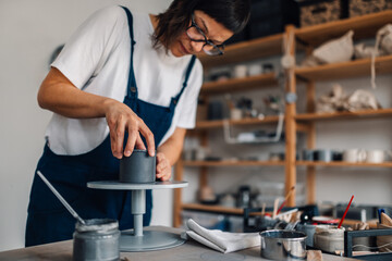 Focused craftswoman standing at ceramics studio and making earthenware