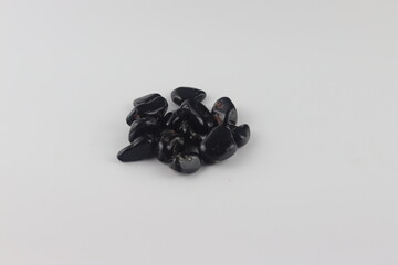 Black onyx tumbled stones on white background. Hand is holding several pieces of polished black onyx, against a white background.