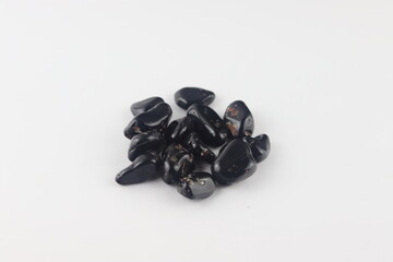 Black onyx tumbled stones on white background. Hand is holding several pieces of polished black onyx, against a white background.