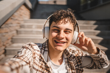 Self portrait of young happy man sit on the stairs with headphones