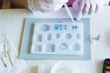Children's hands in gloves fill a mold for making a puzzle piece with epoxy resin