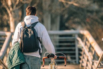young man or student on the street with vintage bicycle at sunset with his back to him