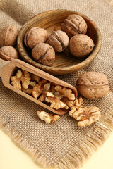 Bowl and scoop of tasty walnuts on yellow background