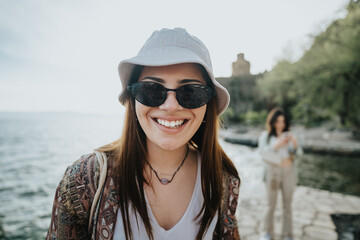 Close-up of a happy girl wearing a bucket hat and sunglasses, expressing joy by the waterfront.