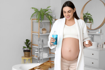 Young pregnant woman with mouth rinse in bathroom