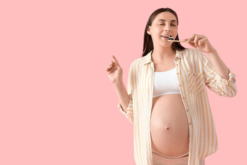 Young pregnant woman brushing teeth on pink background