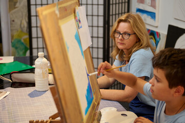 Children painting with teacher in art class, learning to draw and paint together