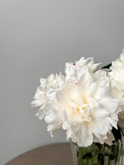 Fading buds of beautiful white peonies in a vase. Fallen flower petals on the table in a vase