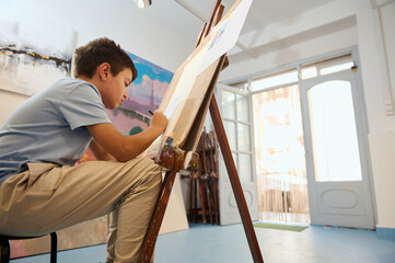 Young boy drawing on easel in art class workshop