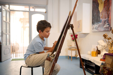 Young boy participating in art class drawing on an easel, learning and creating in a workshop
