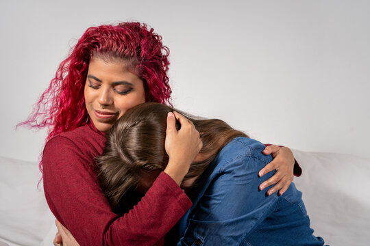 Mujer reconfortando y consolando a su amiga con un abrazo y acariciando su cabeza, mientras est&aacute;n sentadas en un sof&aacute;