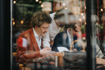 Group of professionals having a business meeting at a trendy cafe, discussing ideas and collaborating on a project with documents and laptops.
