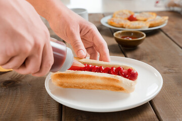 Woman adding ketchup to a hot dog in kitchen