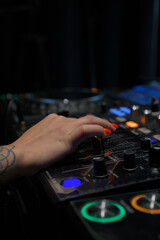 Close-up photo of a female DJ's hand adjusting controls on a professional audio mixer, showcasing vibrant nail art and high-tech equipment.
