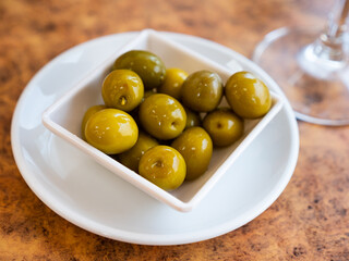 Appetites are waiting on table, light snack - bowl with pickled green olives. Traditional vegetable addition to main dishes, snacks and alcoholic beverages