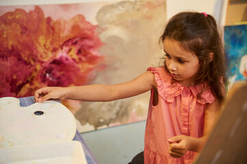 Kids have art class, drawing, painting with teacher in workshop. A young girl engaged in a creative activity with vibrant artwork in the background.