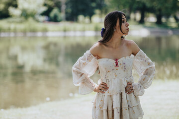 A beautiful young woman stands by a serene lake in a park, dressed in a stylish floral dress,...