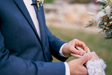 Groom puts the ring on the bride hand. Cropped. Faceless