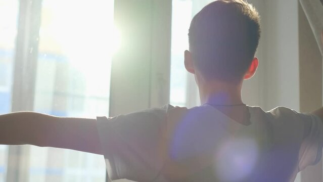 Waking up young man parting the curtains in the morning letting sunlight into the room