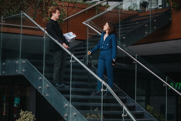 Two businesspeople in formal attire conversing on a modern office staircase, engaged in a professional discussion.