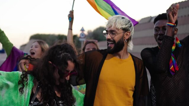 Young LGBT community joyful diverse friends strolling together on day gay pride parade city. Happy rainbow colorful people enjoy smiling hugging walking outdoors. Generation z and sexual liberation. 