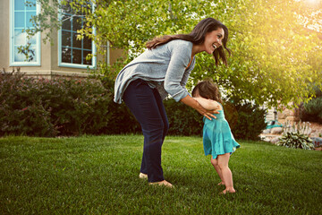 Fototapeta premium Mother, child and happy with playing in garden for fun activity, bonding and smile outdoor in home. Family, woman and daughter on grass of house with care, explore and healthy relationship in nature