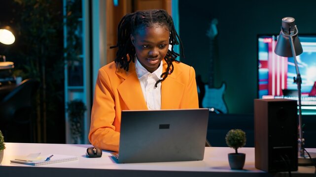 Dedicated woman diligently typing on laptop in the comfort of her home office, writing school essay to finish university homework. African american student working on improving knowledge. Camera A.