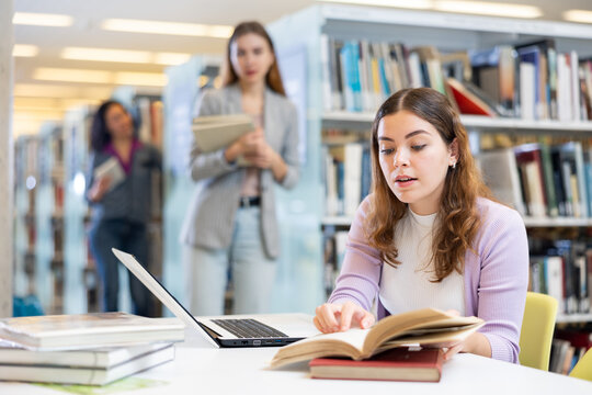 Portrait of young woman studying at library using books and laptop