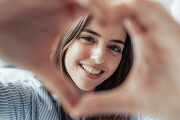 Beautiful woman showing heart sign with folded fingers smiling looking at camera, head shot...