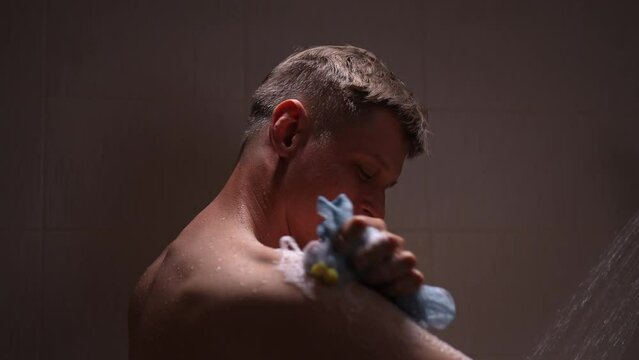Closeup of young adult sexy bare caucasian man washing body with gel foam holding sponge puff taking shower in bathroom, enjoying everyday hygiene routine for fresh clean skin care, slow motion.