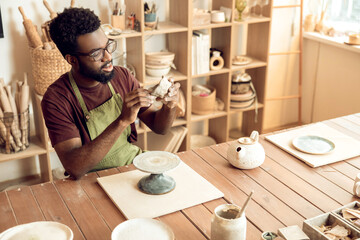 Dark-skinned man at the table with piece of clay in hands