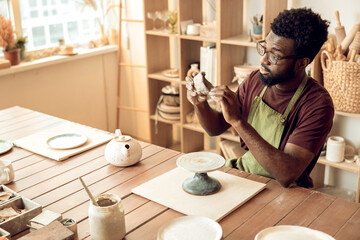 Fototapeta premium Dark-skinned man at the table with piece of clay in hands