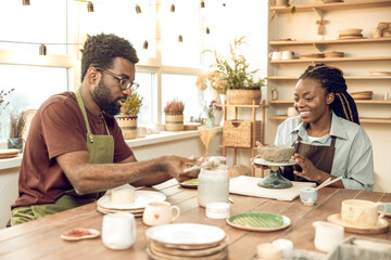 Cute dark-skinned woman having a pottery master class with a male sculptor