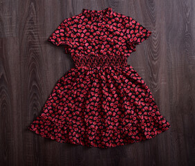 A child's floral dress in deep red on a wooden background.
