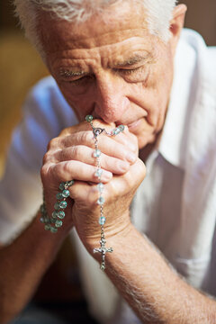 Senior man, catholic and praying in home with rosary or hail mary for God, Jesus and heaven. Elderly person, praise and worship with crucifix for faith, religion and as Christian by apostles creed