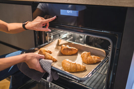 Close up picture of womans hand taking the tray with croissants out of the oven