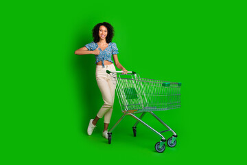 Full length portrait of pretty young girl market trolley thumb up wear top isolated on green color...