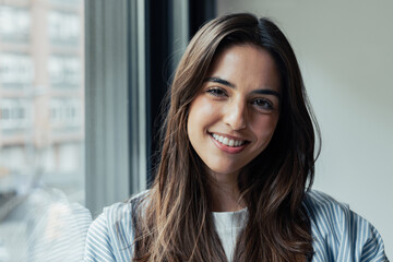 Fototapeta premium Head shot portrait confident positive woman with healthy toothy smile looking at camera, standing near window, successful happy businesswoman entrepreneur student posing for profile picture.