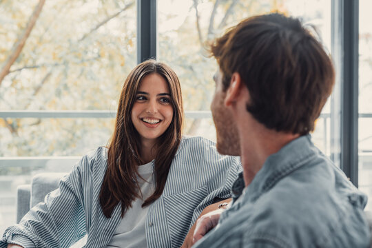 Young happy couple having fun talking laughing relaxing at home on couch, boyfriend embracing girlfriend telling funny joke sitting on sofa, humor in relationships, enjoying weekend together.