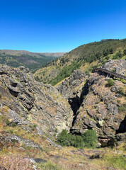 A serene valley with a wooden path, embraced by rocky cliffs. Guarda, Portugal.