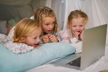 Happy, girls and laptop for streaming tv or watching movies before bedtime for relax and comfort. Exited, sisters or friends and computer for bonding with entertainment and film in blanket fort