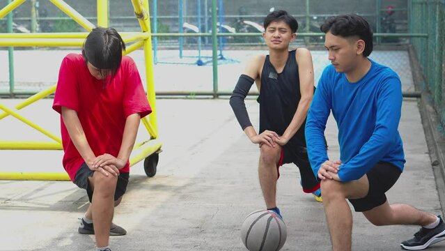 Asian Basketball Players Stretching Legs And Warming Up Before Playing On An Outdoor Court 