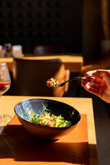 person enjoys a meal of fresh seafood salad with greens and vegetables, taking a bite with a fork