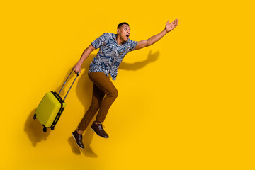 Full length photo of funky cool guy dressed print shirt holding baggage jumping running empty space isolated yellow color background