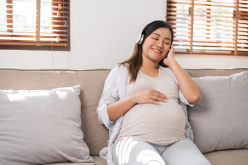 Relaxed Pregnant Woman Sitting on Sofa in Modern Living Room, Listening to Music with Headphone, Enjoying a Peaceful Moment, Expecting Mother in Comfortable Home Environment