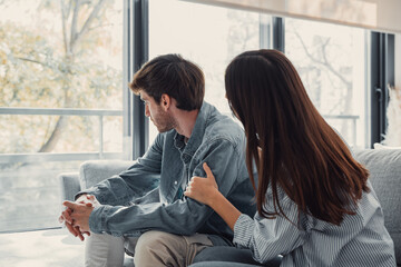 Attractive man is depressed, sitting on the couch ignoring woman, having a dispute with wife or boyfriend, looking desperate and hopeless, having unresolved problem or question.