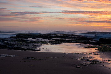 Sunrise over breaking waves beach orange yellow clouds	