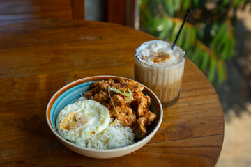 salted egg chicken rice bowl with egg served on blue bowl, over wooden table surface, in cafe environment