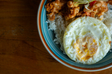 salted egg chicken rice bowl with egg served on blue bowl, over wooden table surface, in cafe environment