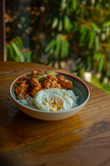 salted egg chicken rice bowl with egg served on blue bowl, over wooden table surface, in cafe environment